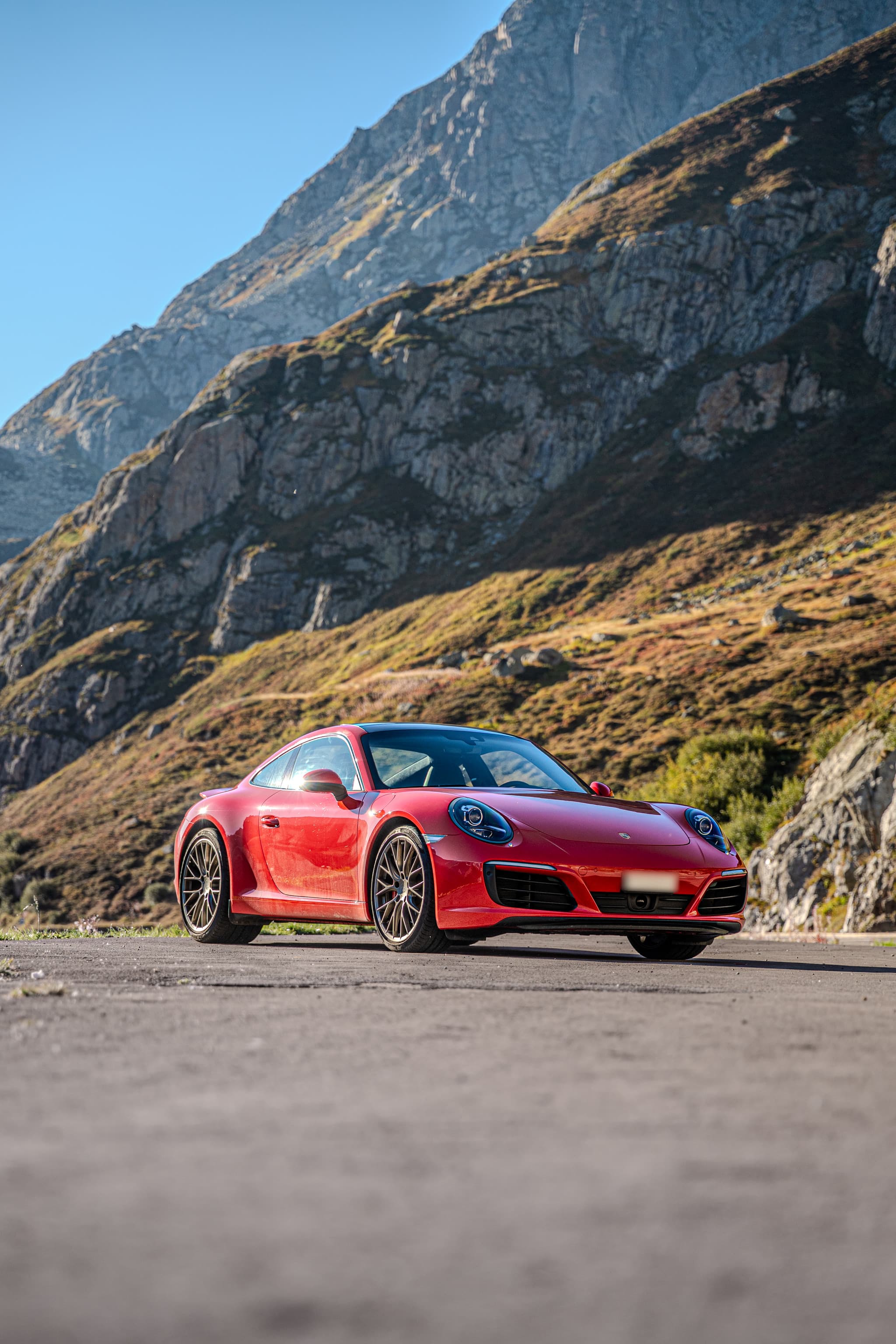 Red Porsche 911 Carrera S Coupé, front three-quarter view on a pass road below tall rock faces